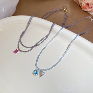 Detailed close-up of beaded necklaces with heart and square gemstone pendants in a ceramic dish