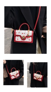Close-up of white cherry print handbag with red woven handle and gold petal clasp detail