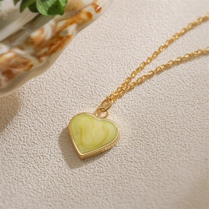 Golden necklace with a heart-shaped yellow-green pendant shown on a white fabric surface