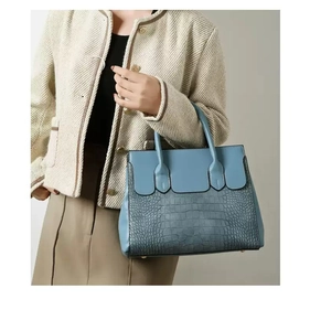 Detail view of the smog blue tote bag featuring crocodile embossed texture and metal base feet