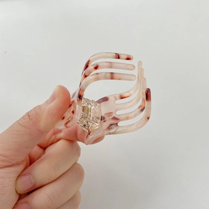 Detail view of a tortoise shell patterned bow hair claw clip held to show size and texture