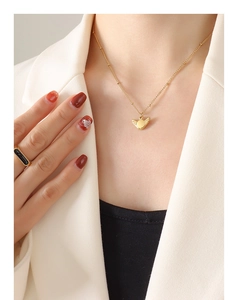 Detail view of a gold wing pendant necklace and black stone ring on a model in a white blazer