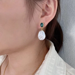 Baroque pearl earrings with green gemstone in a drop design on a female model