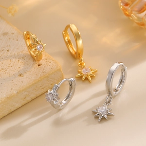 Detailed view of asymmetric star earrings with zircon inlay on beige stone background