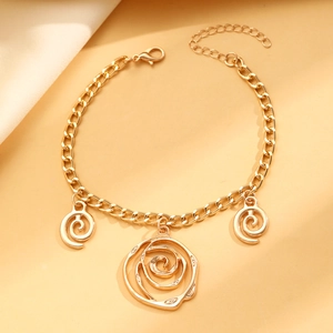 Detail of a golden chain bracelet with rose and spiral charms on soft fabric background