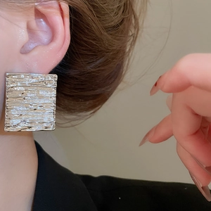 Close-up of square silver metallic stud earring with brushed texture on model