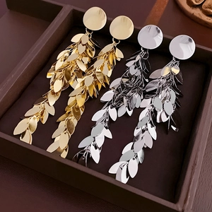 Detailed view of gold and silver layered leaf tassel earrings on a dark wood tray