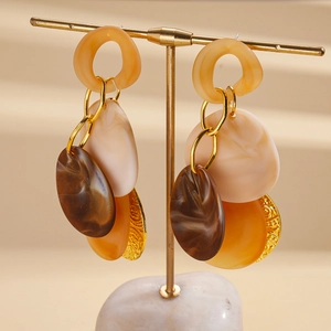 Detail view of acrylic geometric layered drop earrings featuring gold textured metal discs