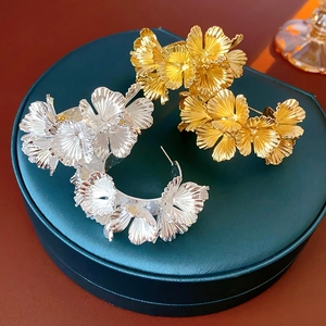 Detailed view of large gold and silver metallic floral earrings on a green jewelry box