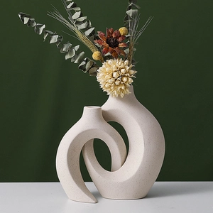 Artistic beige ceramic vase with abstract intertwined rings and dried eucalyptus leaves