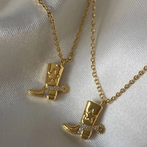 Gold plated cowboy boot pendant necklace with white crystals on white silk background
