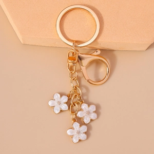 Close-up of golden keychain with three white cherry blossom charms on a metal chain