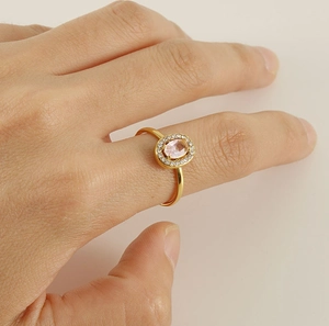 Close-up of golden ring featuring an oval pink gemstone with a white diamond halo