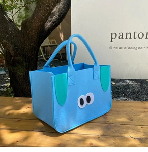 Blue felt tote bag with cute cartoon animal ears and eyes on a wooden outdoor bench