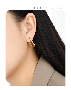 Close-up of golden geometric twisted triangle earrings worn by a model for a stylish look