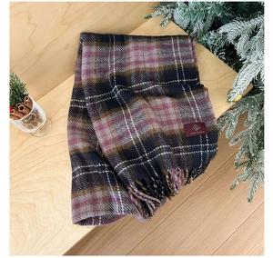 Detail of red plaid scarf with tassel fringe and logo tag on a wooden surface