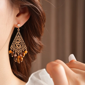 Detail of golden hollow rhombus earrings with tiger eye stone tassels on female model