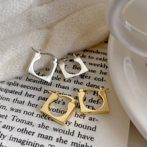 Detailed view of silver and gold square hoop earrings on a vintage book page