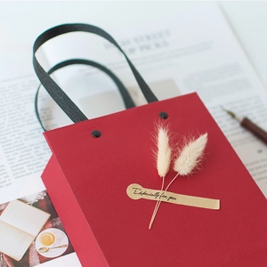 Elegant red gift bag with rabbit tail grass and gold label on aesthetic background