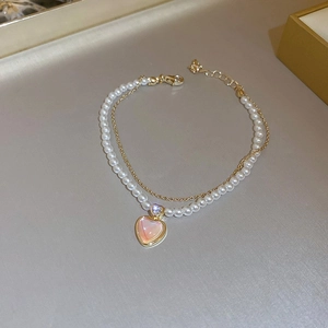Macro detail of gold-plated double-layer bracelet with cat eye heart and pearls