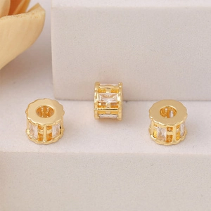 Close-up of golden hollow grid cylindrical charms with sparkling zircon stones