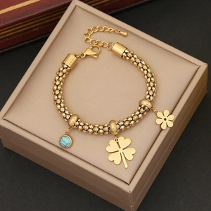 Detail of golden stainless steel bracelet with clover, flower charms and turquoise bead