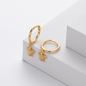 Close-up of golden turtle drop earrings on white geometric blocks with detailed texture