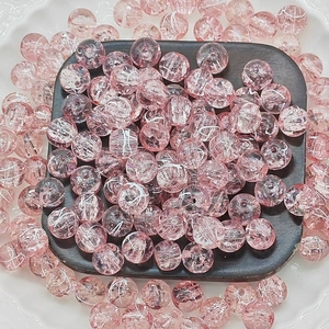 Macro shot of pink cracked glass beads with icy textures in a decorative display tray