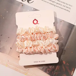 Close-up of cream and pink satin scrunchies set on white display card with glossy texture