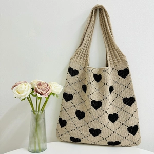 Beige knitted tote bag with black heart patterns and diamond texture in a clean setup