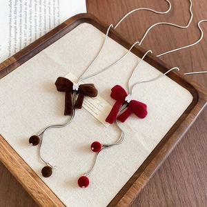 Detail view of brown and red velvet bow necklaces with cubic zirconia on wooden tray