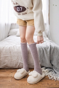 Close-up of soft lavender plush knee-high socks paired with cozy beige fleece slippers