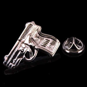 Dettaglio spilla a forma di pistola argento con texture meccanica e chiusura a farfalla