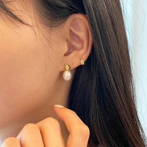 Detail of freshwater pearl drop earrings with gold hoops worn on a model's ear