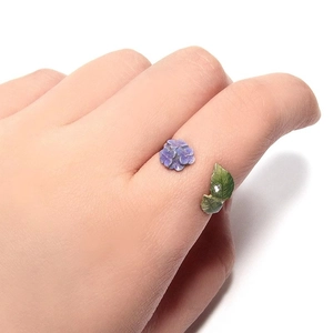 Detail of adjustable flower ring with purple petals and green leaf on hand