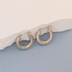 Detail view of silver oval hoop earrings with woven texture on white stone background