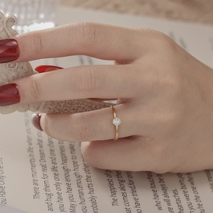 Close-up of minimalist gold ring with clear gemstone on hand with a blurred book background