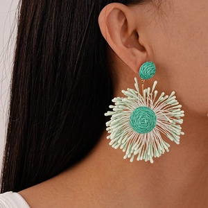 Close-up of green hand-woven floral bohemian drop earrings worn on a model's ear