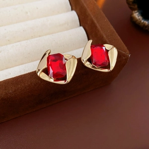 Close-up of geometric gold earrings with red rectangle gemstones in a brown velvet box