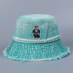Close-up of bear embroidery and frayed edges on washed denim bucket hat in light blue