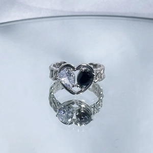 Detail of silver heart ring with clear and black teardrop stones on a reflective surface