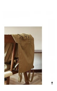 Détail du tablier plissé kaki imperméable suspendu sur une chaise en bois rétro