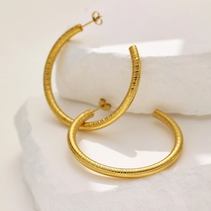 Macro shot of gold-plated hollow hoop earrings with textured snake pattern surface