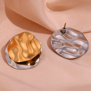 Detail of two-tone wave earrings on silk showing gold and silver layered texture