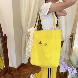 Detail of yellow canvas tote bag featuring butterfly print and white lace bow accessory