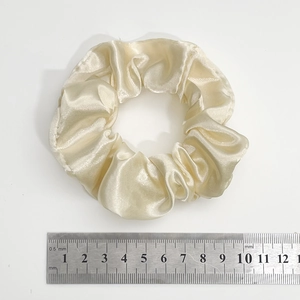 Top view of beige satin scrunchie showing 10cm diameter measurement on a scale