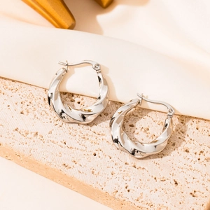 Polished silver stainless steel twist hoop earrings on elegant textured travertine surface