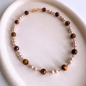 Tiger eye stone and pearl beaded necklace with gold buckle on elegant beige tray