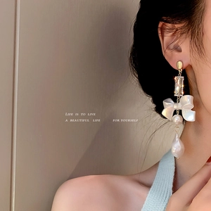 Elegant gold bow earrings with crystal links and baroque pearls worn by a model