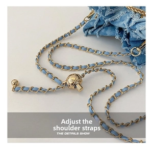 Detail of blue denim bag featuring gold chain strap with adjustable metal ball
